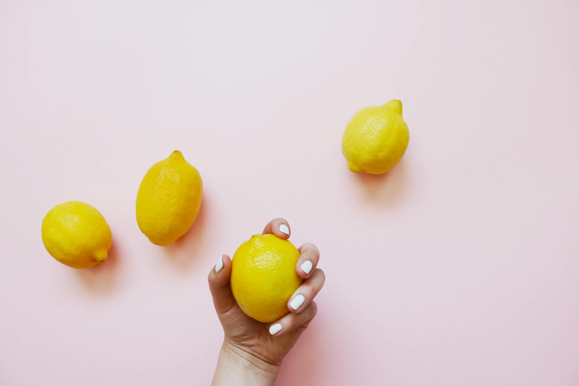 A hand holding a fresh lemon on a soft pink background, symbolizing intimacy and refreshment in relationships.