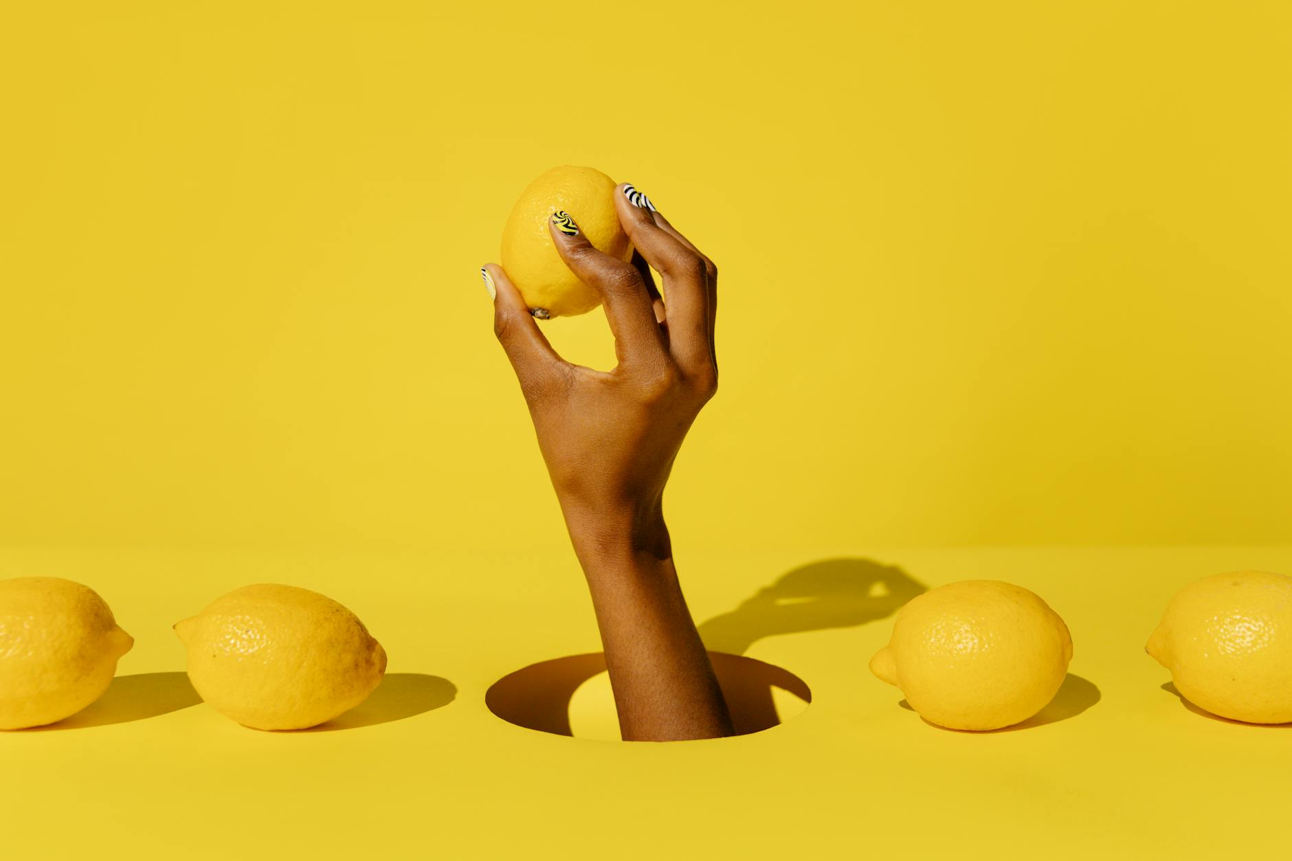 Une main tenant un citron frais vibrant sur un fond jaune vif
