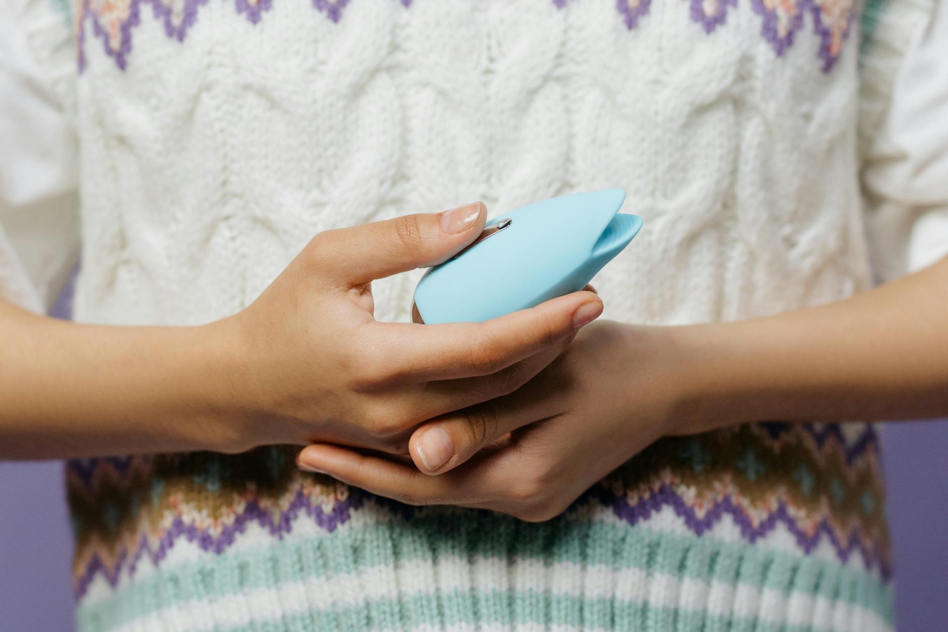 Gros plan de mains tenant un vibromasseur bleu contre un pull tricoté.