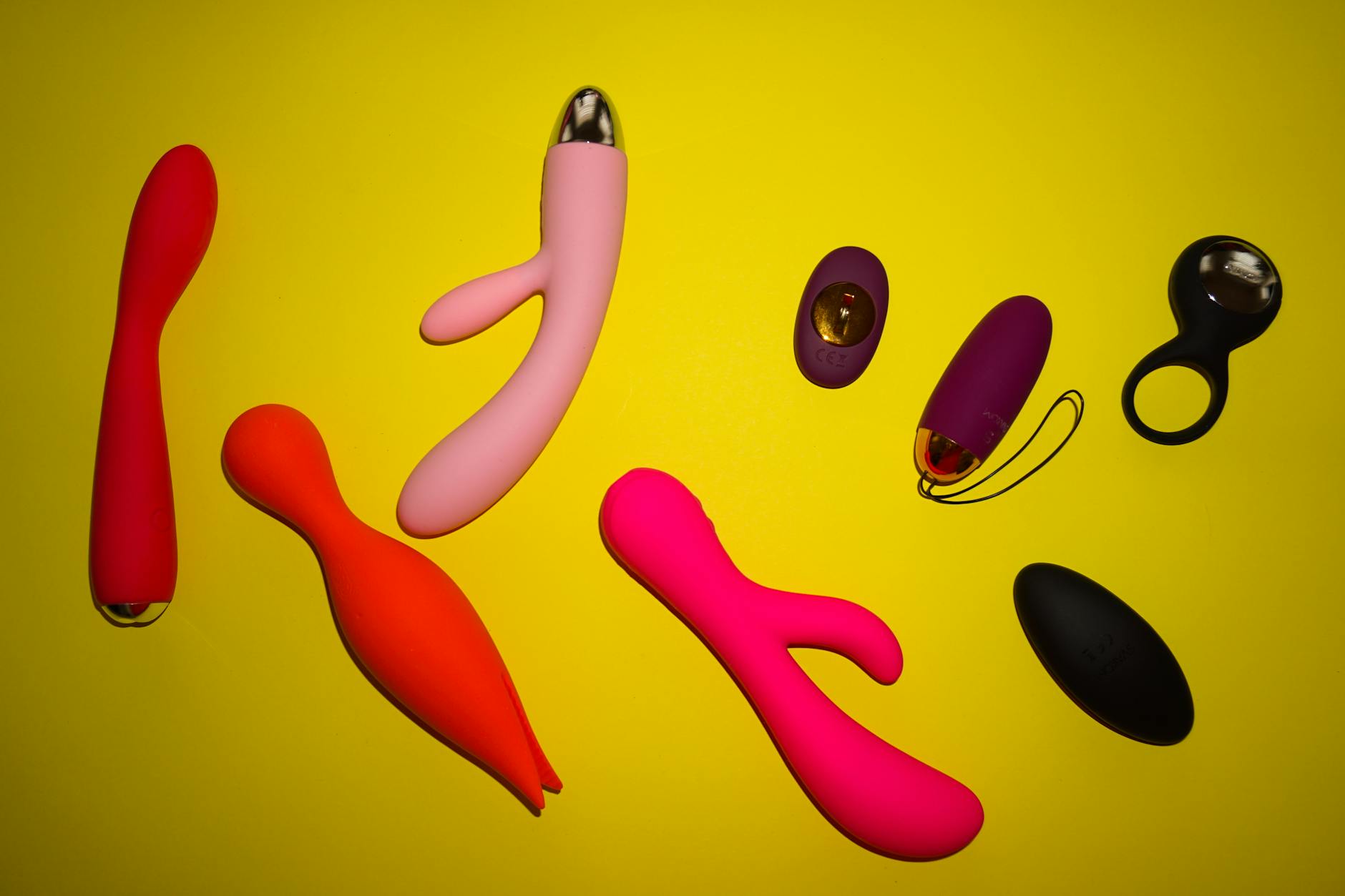 A vibrant collection of colorful clitoral vibrators and sexual toys arranged on a bright yellow surface