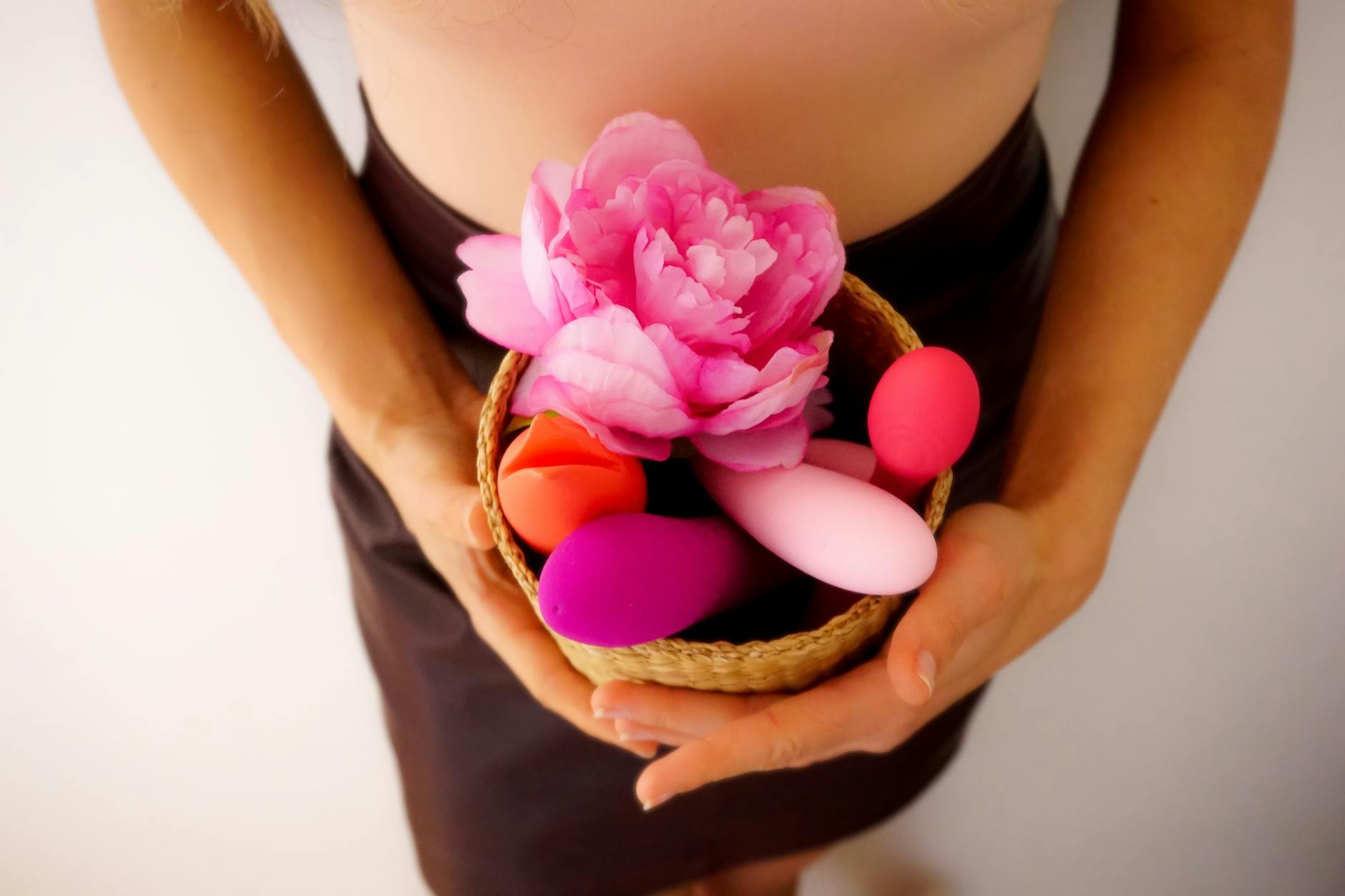 Vibromasseurs colorés, y compris un stimulateur clitoridien, dans un panier rose
